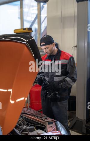 Vertical portrait of male mechanic inspecting engine while working in car repair shop Stock Photo
