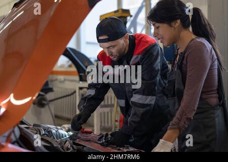 Side view portrait of two mechanics looking under hood inspecting car engine while working in auto repair shop, copy space Stock Photo