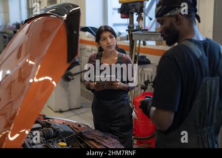 Waist up portrait of female mechanic using digital tablet while inspecting car in auto repair workshop Stock Photo