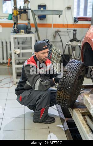 Vertical full length portrait of male mechanic changing tires on car while working in auto repair shop Stock Photo