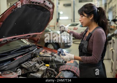 Side view portrait of young female mechanic checking oil levels while repairing car in workshop, copy space Stock Photo
