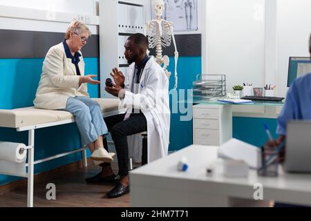 African american therapist doctor discussing sickness symptoms holding pills bottle explaining healthcare treatment to senior woman patient. Medical examination in hospital office. Medicine concept Stock Photo