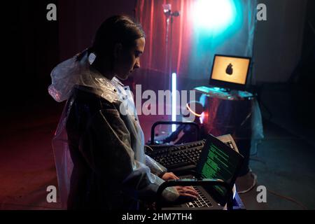 Young woman in raincoat typing on laptop, she developing new program and working with scripts on the screen Stock Photo
