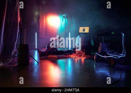 Young woman connecting man with virtual reality while he lying on mattress in dark room Stock Photo