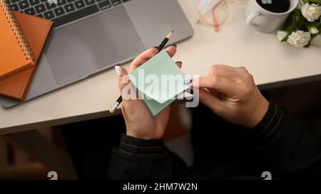 A creative female taking notes on sticky notes or notepad over her modern office workspace. top view Stock Photo