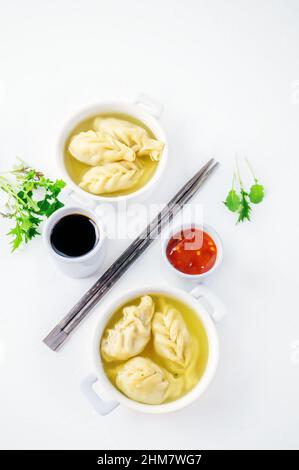 Dumplings are served in white cups with sauces on a serving board . Top view. Copy space. Stock Photo