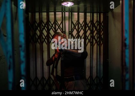 Waist up portrait of tough young woman pointing gun at camera while standing in dark elevator ready to fight, copy space Stock Photo