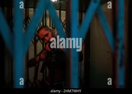 Waist up portrait of tough woman with buzz cut pointing gun at camera while standing in dark room ready to fight, copy space Stock Photo