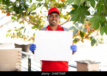 Happy smiling delivery boy with white sign board looking at camera - concept of free and fast home courier service promotion and advertisement Stock Photo