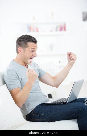 man in exaggerating happy expression in front on laptop Stock Photo
