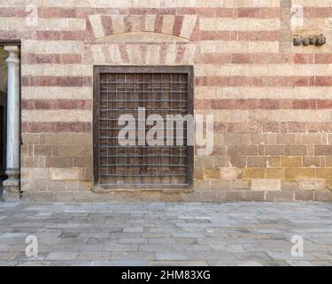 Daylight shot of wooden window with wrought iron grid in a wall decorated with beige and red stones Stock Photo