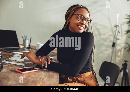 Imaginative young woman smiling in her home office. Happy young photographer thinking of new creative ideas for her project. Artistic female freelance Stock Photo
