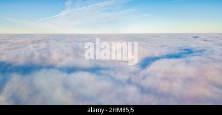 Aerial drone flight over the fog. There are thick clouds of fog below, the sun breaks through the clouds. Stock Photo