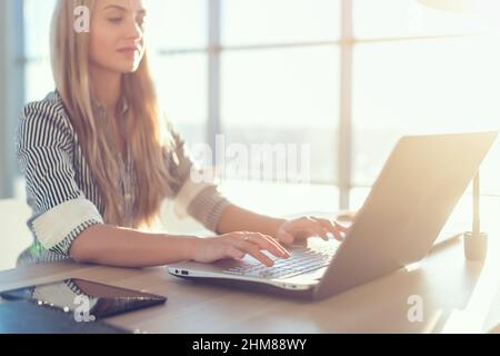 Young beautiful female copywriter typing texts and blogs in spacious light office, her workplace, using pc keyboard. Busy woman working Stock Photo