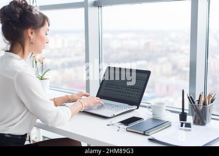 Young businesswoman working in office, typing, using computer. Concentrated woman searching information online, rear view portrait Stock Photo