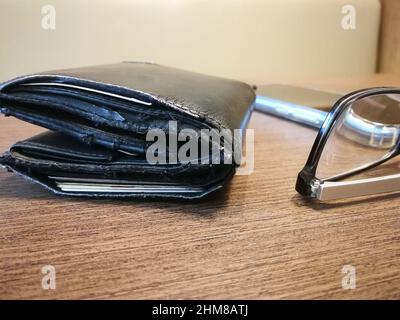 Blurred background of old wallet on the wooden desk with reading glasses and smartphone. Debt concept Stock Photo