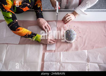 Top view of the work of tailors in the workshop measuring, cutting and sewing clothes from the fabric on the table based on paper template. Stock Photo