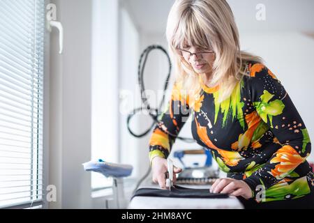 Female tailor cuts fabric with scissors in her own workshop. Stock Photo
