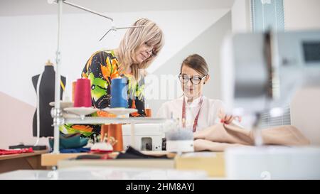 Two generations of female tailors cooperate at work in the small workshop. Stock Photo