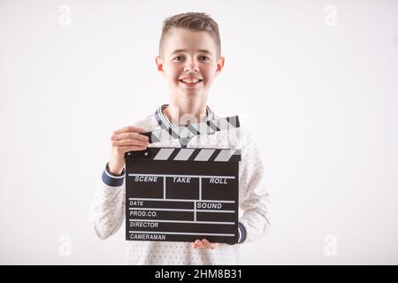 Young boy on an isolated white background holds an open movie clapper board. Stock Photo