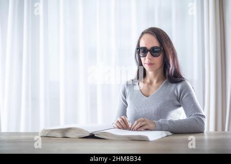 Blind woman reads book in braille on a table in front of her. Stock Photo