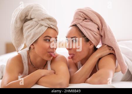 Girls' night for mom and daughter with hair wrapped in towels, sticking their tongues out at each other, having fun. Stock Photo