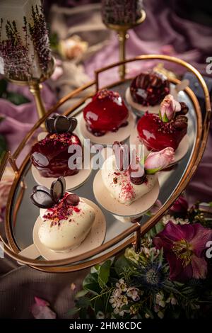 Modern mousse cakes with red and white mirror glaze in the shape of a heart decorated with rose and chocolate. Valentine's day or wedding cake still l Stock Photo