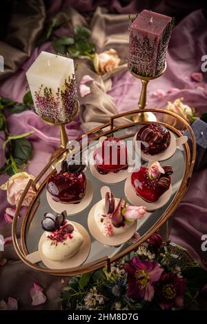 Still life of heart shaped mini cakes decorated with rose, chocolate or macarons Stock Photo