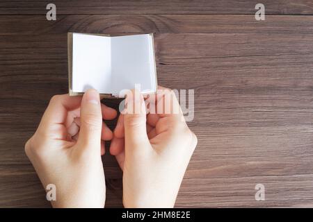 Crop view of female hands holding a miniature book with blank pages against a wooden table background. Education and learning concept. Stock Photo