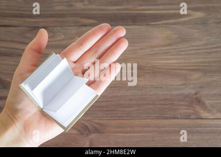 Miniature open book with blank pages on the palm of the female hand against a wooden table background. Education and learning concept. Stock Photo