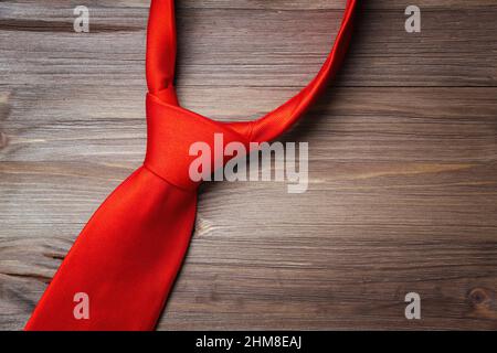 Cropped view of a tied solid red business necktie folded on a wooden background with copy space. Stock Photo