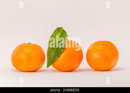 Three mandarin orange citrus, one with green leaf, isolated on white background Stock Photo
