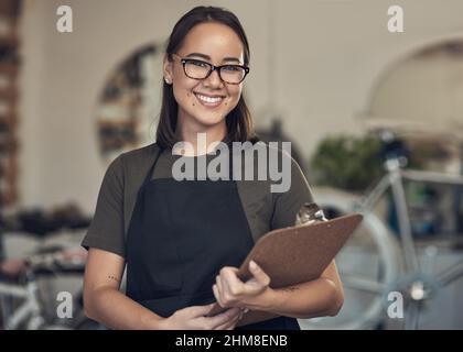 I take pride in my business. Shot of an attractive young woman standing alone in her bicycle shop and holding a clipboard. Stock Photo