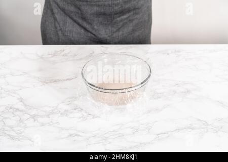 Activating dry yeast in a glass mixing bowl to prepare dinner rolls. Stock Photo