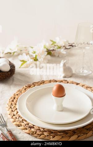 Happy Easter morning, festive dinner with egg, bunny, fresh flowers on white linen tablecloth. Vertical format. Close up. Stock Photo