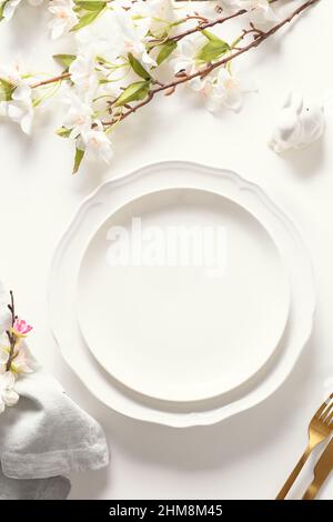 Easter festive dinner with golden eggs, festive tableware and flowers on white background. Top view. Festive tablescapes. Vertical format. Stock Photo