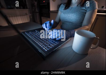 A faceless girl in a medical mask and glasses studies late in the kitchen during quarantine. Unrecognizable woman working remotely from home on a Stock Photo