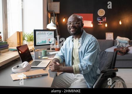 Portrait of African man with disability sitting on wheelchair and smiling at camera while working at home Stock Photo