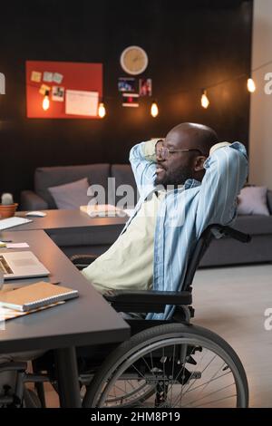 African man sitting on wheelchair at his workplace, he resting after work at home Stock Photo