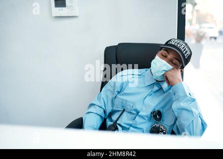 When fighting crime turns into fighting fatigue. Shot of a masked young security guard sleeping at a desk in an office. Stock Photo
