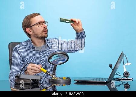 Portrait of man in glasses and checkered shirt attentively looking at motherboard isolated over blue background Stock Photo