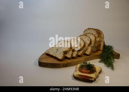 Sliced ​​wholemeal bread on a wooden board, dill, tomato and sandwich with cheese. Stock Photo