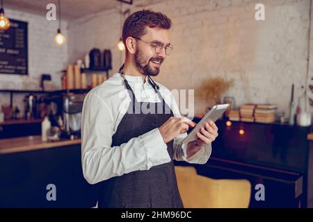 Joyful male barista using tablet computer in coffee shop Stock Photo