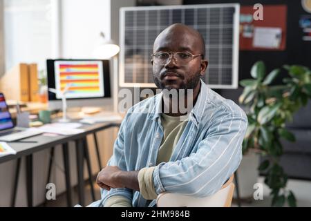 Portrait of African businessman in eyeglasses sitting on chair and looking at camera during his work at office Stock Photo