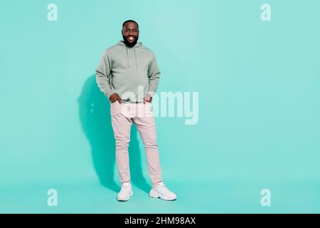 Full length body size view of attractive cheerful guy holding hands in pockets isolated over bright teal turquoise color background Stock Photo