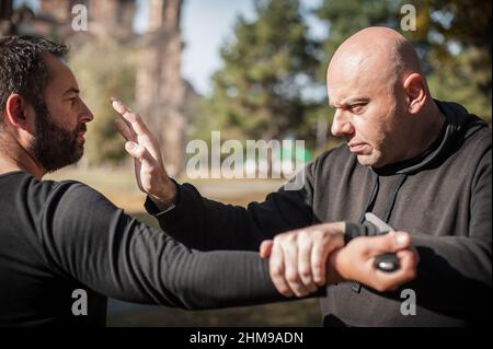 Knife threat. Kapap instructor demonstrates martial arts self defense disarming technique against knife attack. Weapon disarm training. Demonstration Stock Photo