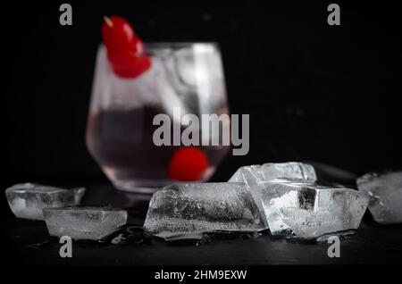 Ice Cubes with Blurred Cocktail and Red Cherries on Black Background Horizontal Stock Photo