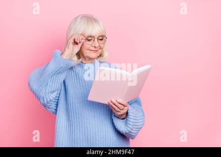 Portrait of attractive cheery focused smart grey-haired woman reading book touching specs isolated over pink pastel color background Stock Photo