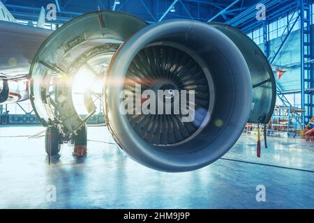 Jet engine with open hood covers on maintenance, illuminated by bright light from behind the hangar gate Stock Photo