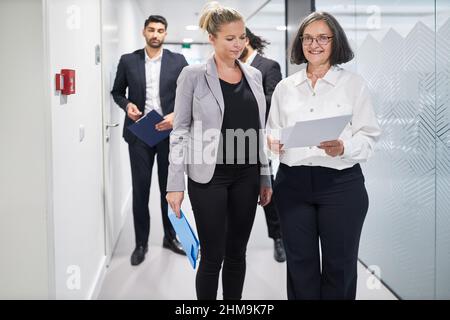 Two business women and colleagues are walking with documents on the corridor of an agency or company Stock Photo